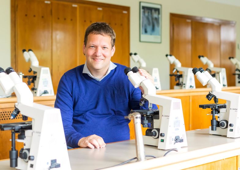 Prof. Dr. Folrian Hansmann sitzt vor einem Mikroskop