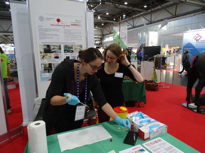 zwei Personen an einer Station am Messestand, die einen Blutausstrich üben