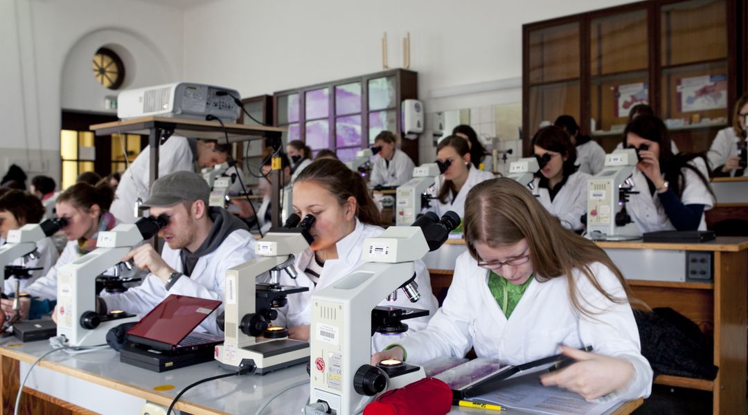 Foto: Studierende im Kittel beim Mikroskopieren im Hörsaal