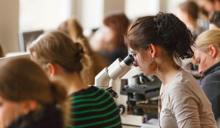 Foto: Studentinnen sitzen im Hörsaal und schauen durch das Mikroskop